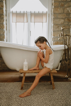 Enfant appliquant le lait hydratant Fleurs de Peau près d’une baignoire