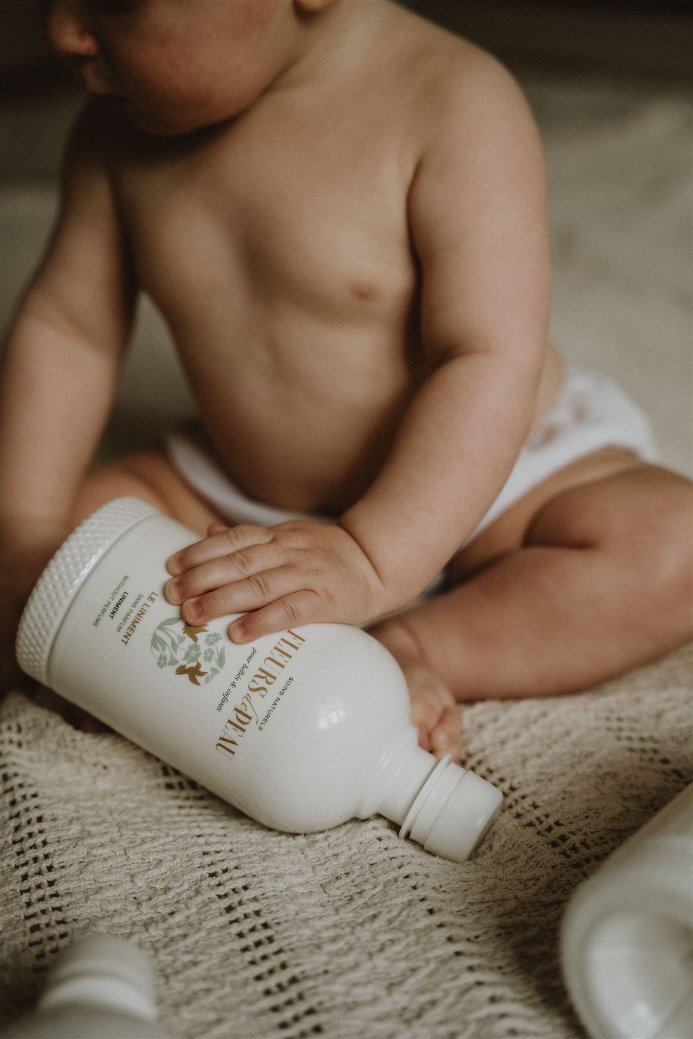 Bébé tenant une bouteille de liniment Fleurs de Peau