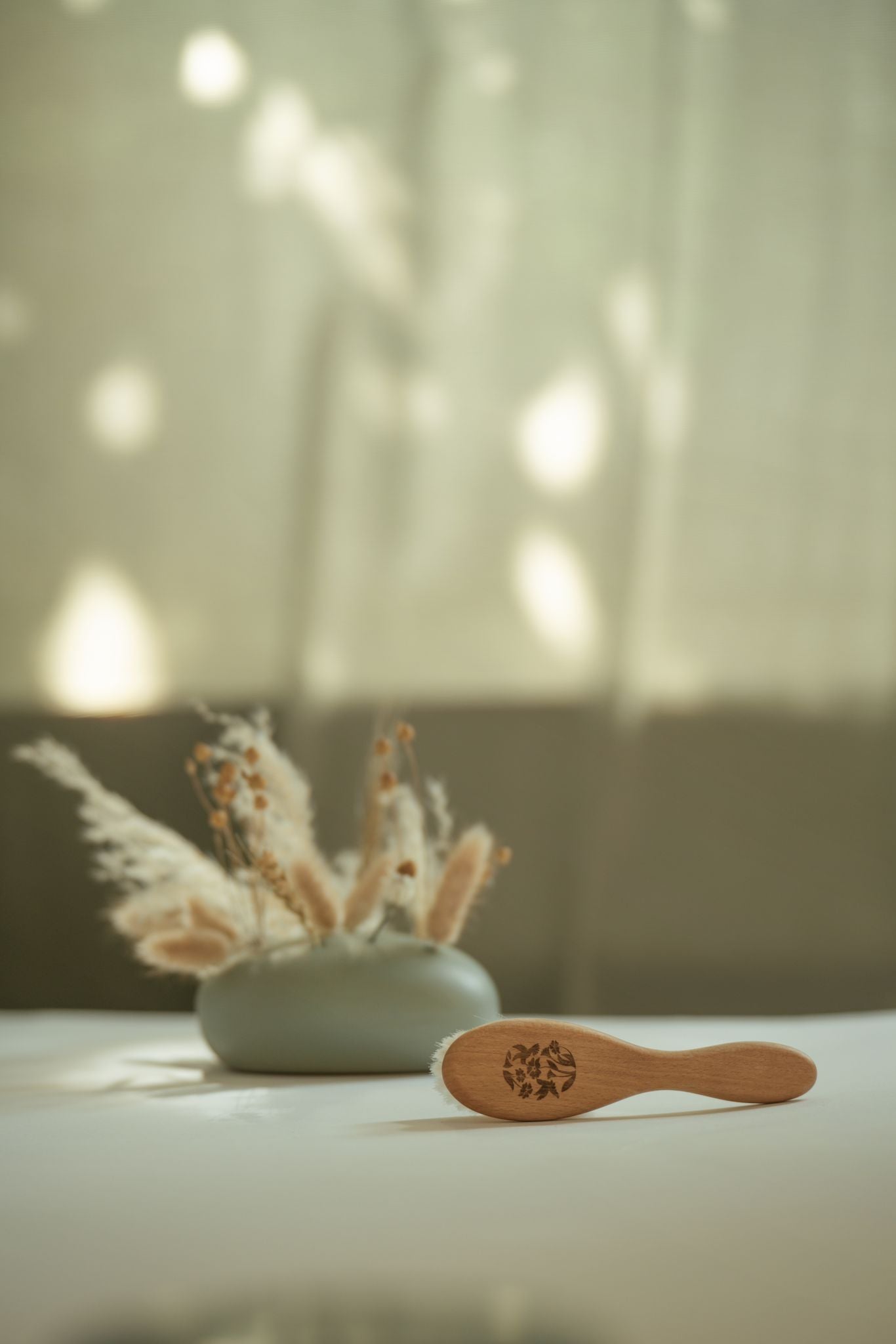 Brosse à cheveux bébé posée à côté d’un vase de fleurs séchées
