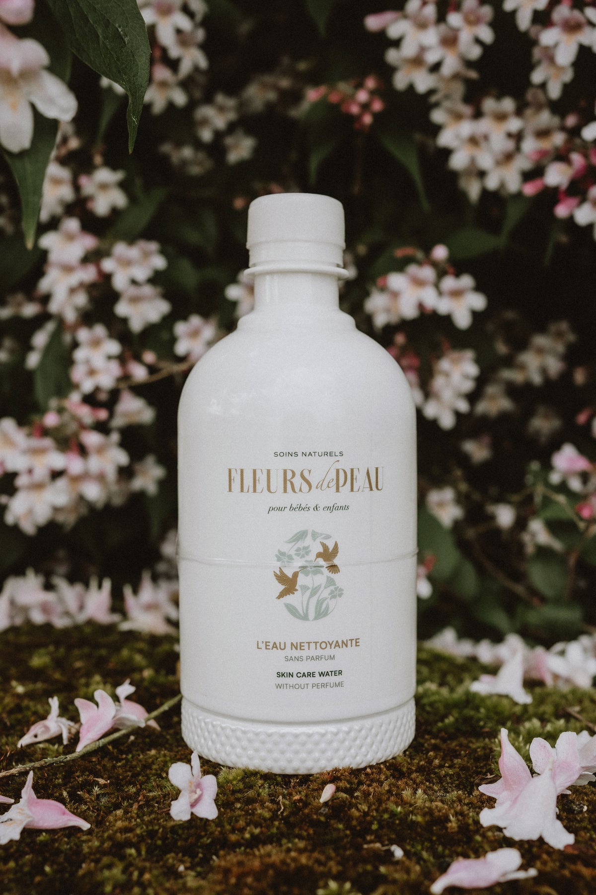 Bouteille d'eau nettoyante Fleurs de Peau posée sur de l'herbe avec des pâquerettes