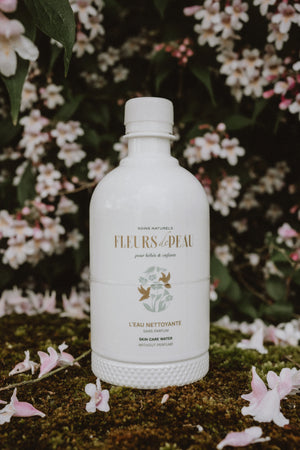Bouteille d'eau nettoyante Fleurs de Peau posée sur de l'herbe avec des pâquerettes