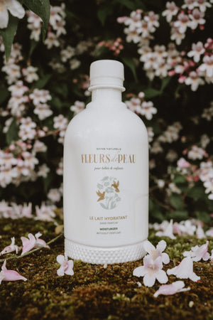 Flacon de lait hydratant Fleurs de Peau entouré de fleurs naturelles