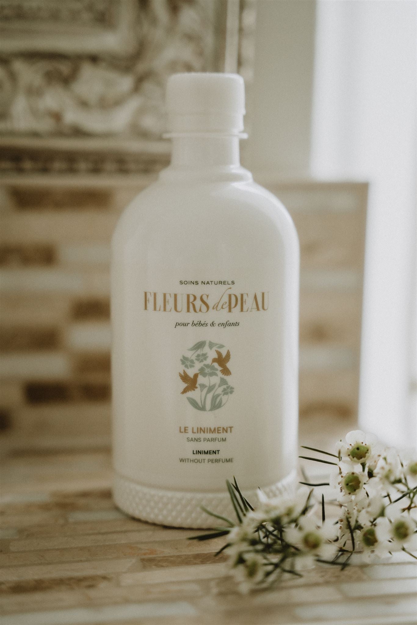 Bouteille de liniment bébé Fleurs de Peau posée avec des fleurs blanches