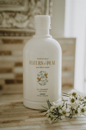 Bouteille de liniment bébé Fleurs de Peau posée avec des fleurs blanches
