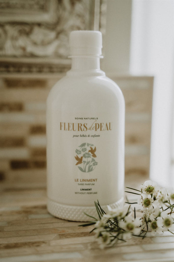 Bouteille de liniment bébé Fleurs de Peau posée avec des fleurs blanches